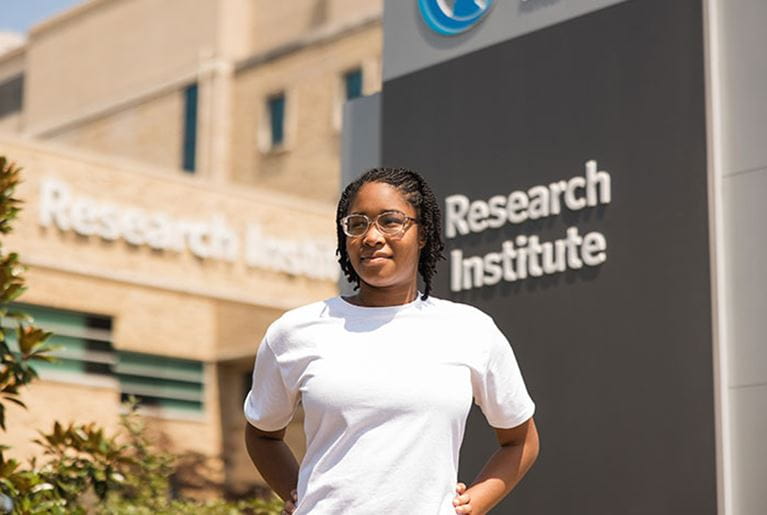 Teen girl standing in front of the Research Institute sign.