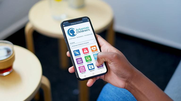 Person holding a mobile phone displaying the Arkansas Children’s app.