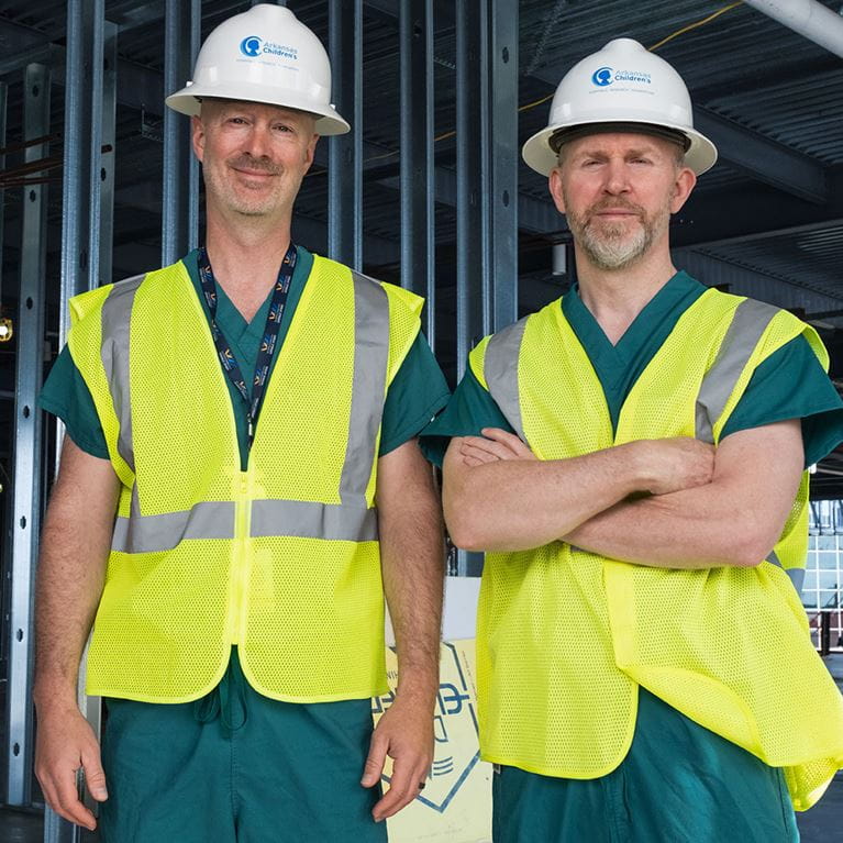 Two physicians wearing white hard hats standing in construction zone.