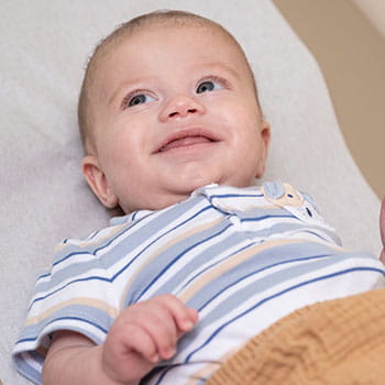 Smiling baby boy wearing striped shirt and tan pants.
