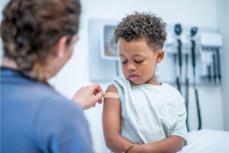 Male toddler in hospital gown getting band-aid on upper arm.
