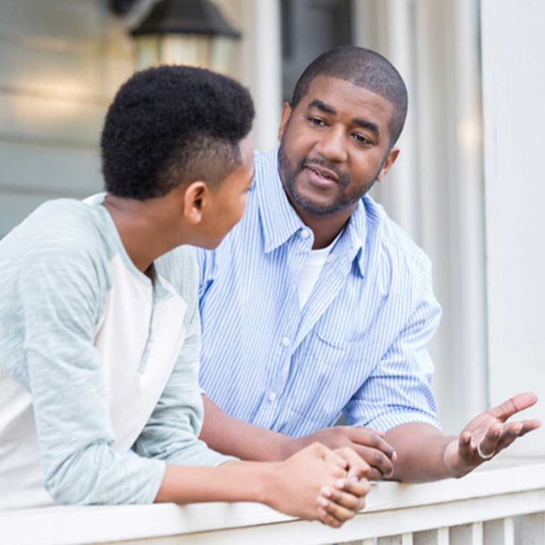 Father and son talking outside on porch.