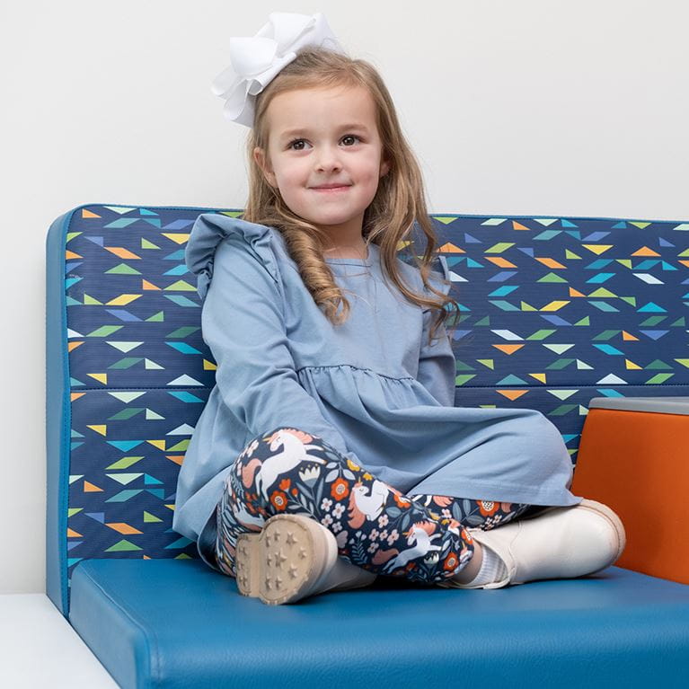  Female patient with white bow sitting on blue couch in waiting room.
