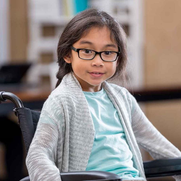 Girl wearing glasses sitting in wheelchair.