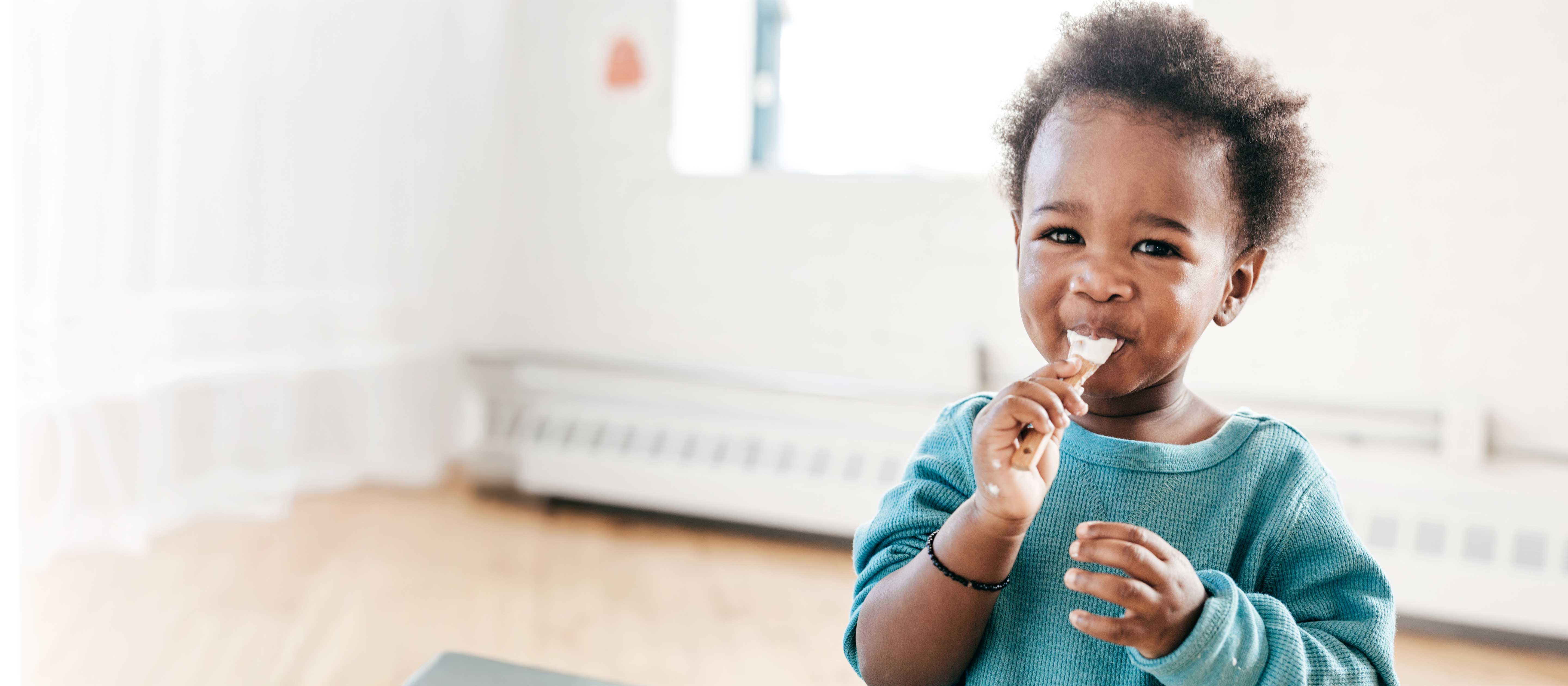 Toodler in green sweater enjoying a spoon of yogurt.