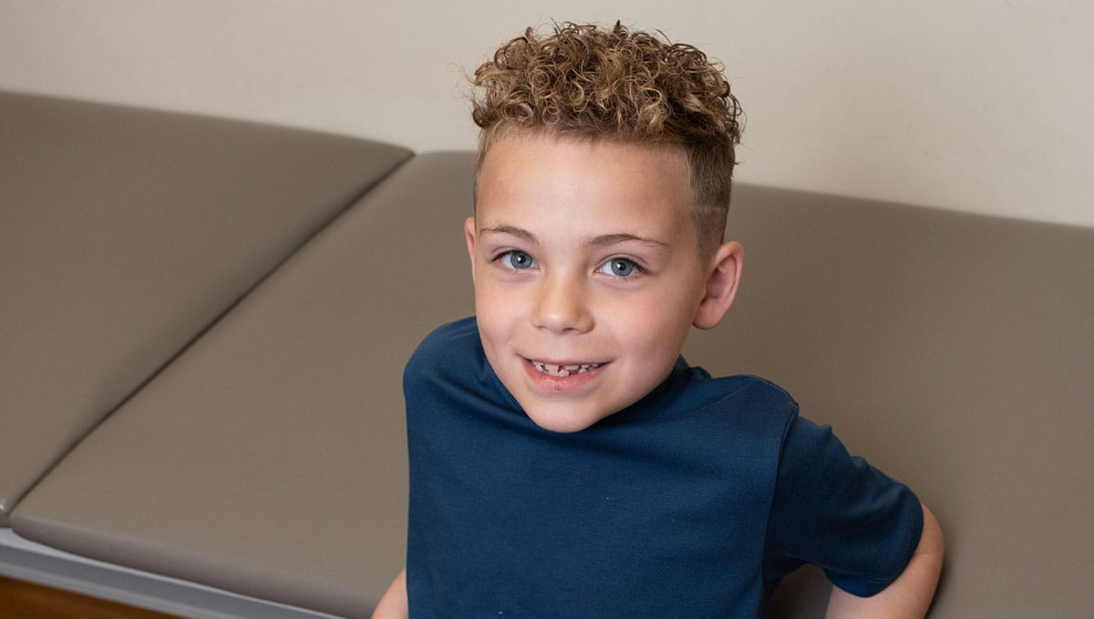 Smiling young blonde boy in clinic wearing navy blue shirt. 