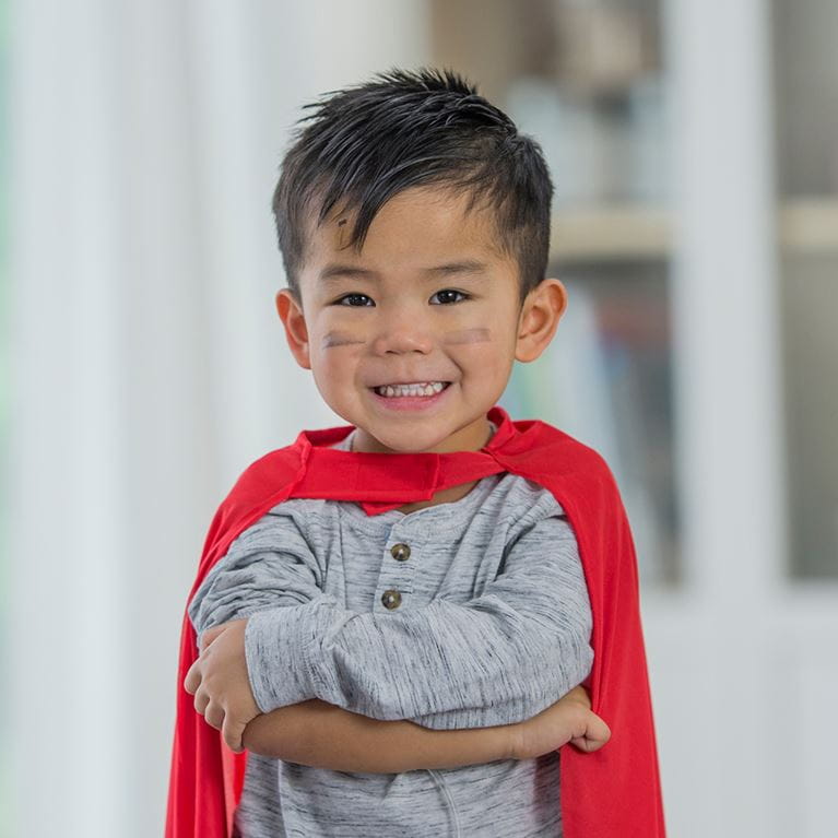 Boy in hallway smiling and wearing red cape