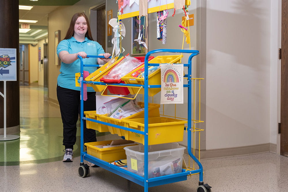 Arkansas Children's volunteer pushing an activity cart.
