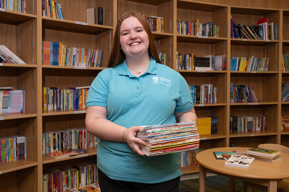 Arkansas Children's volunteer holding books in library.