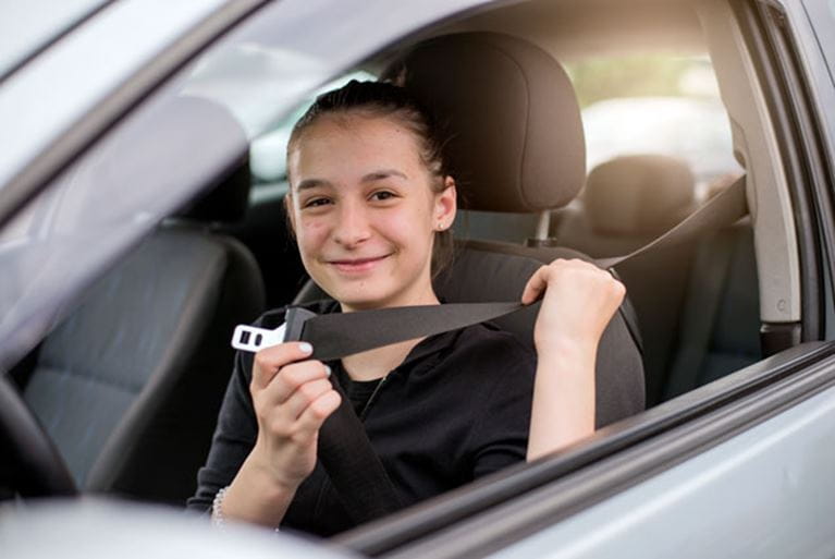 Smiling teen driver fastening seatbelt.
