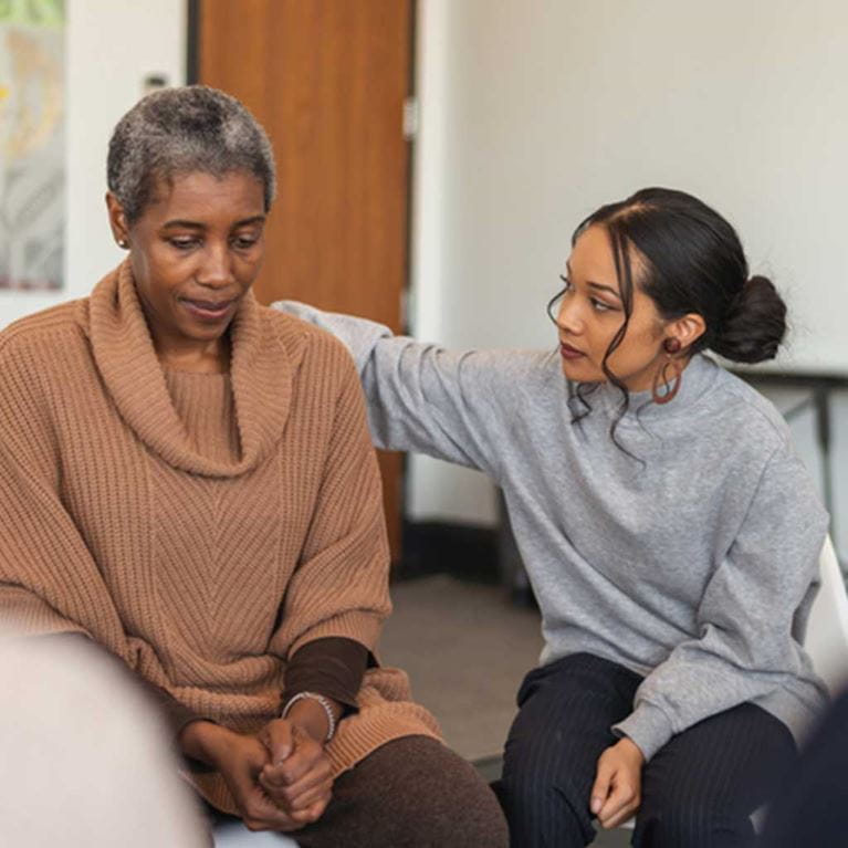 Two women sitting down comforting each other.