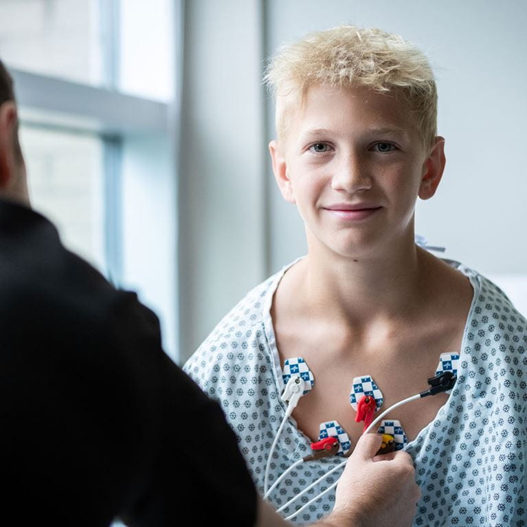 Tween boy with blonde hair in hospital gown.