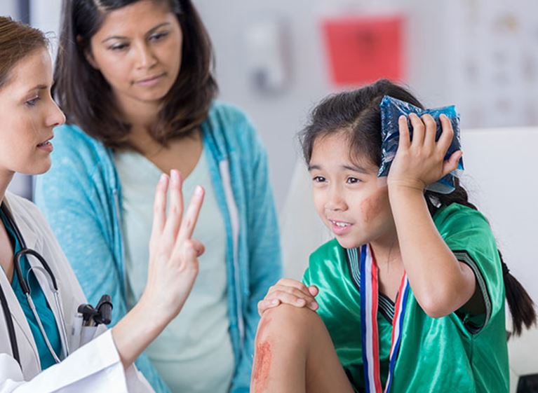 Healthcare provider examines a child athlete using an ice pack, with an adult nearby.