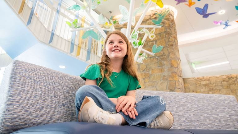 Smiling girl sitting cross-legged in the lobby of Champions Pavilion.