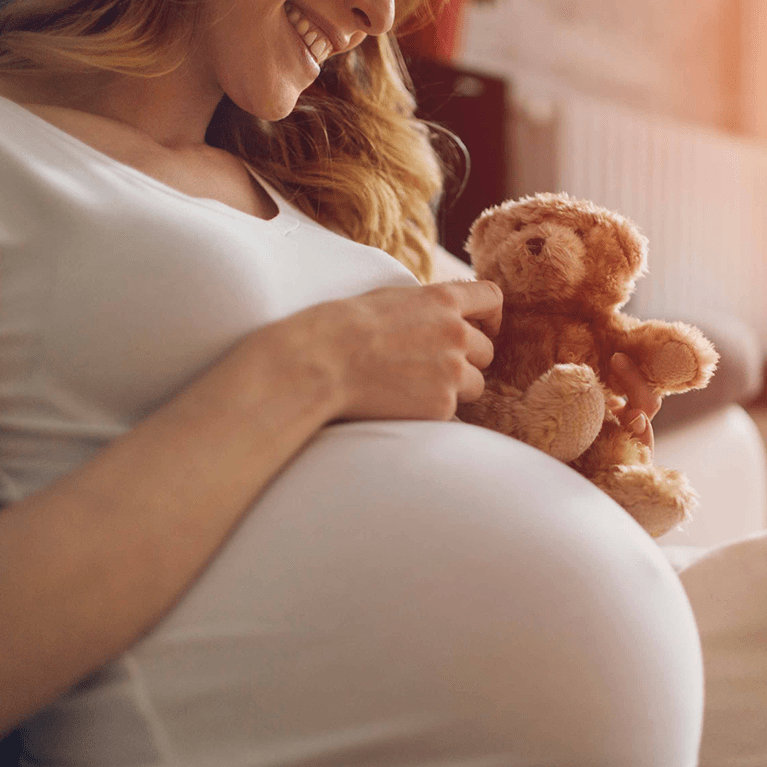 Pregnant woman holding teddy bear.
